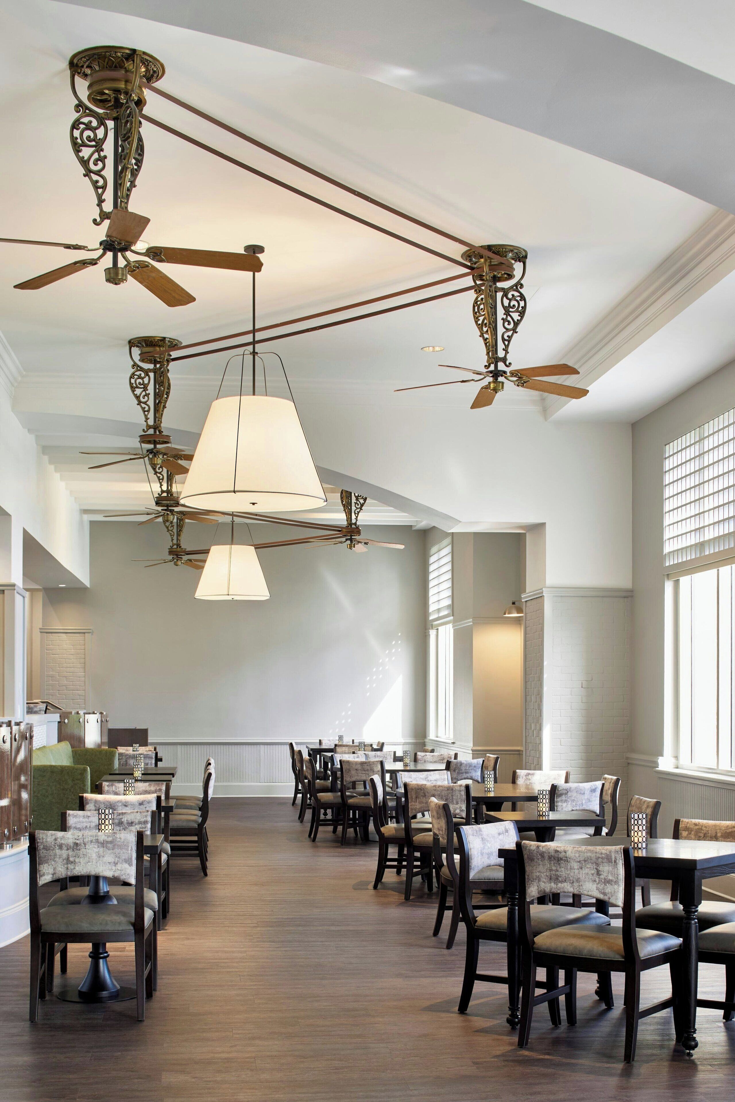 A spacious dining area with high ceilings, ornate ceiling fans, and large windows allowing natural light.