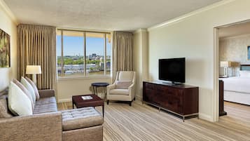 Ein Hotelzimmer mit großem Fenster, einer Couch, einem Sessel, einem Fernseher, einem kleinen Tisch und einem Bett.