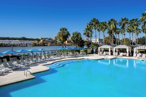 A swimming pool with lounge chairs and umbrellas, surrounded by palm trees and buildings in the background. - The Westin Savannah Harbor Golf Resort & Spa (Savannah)