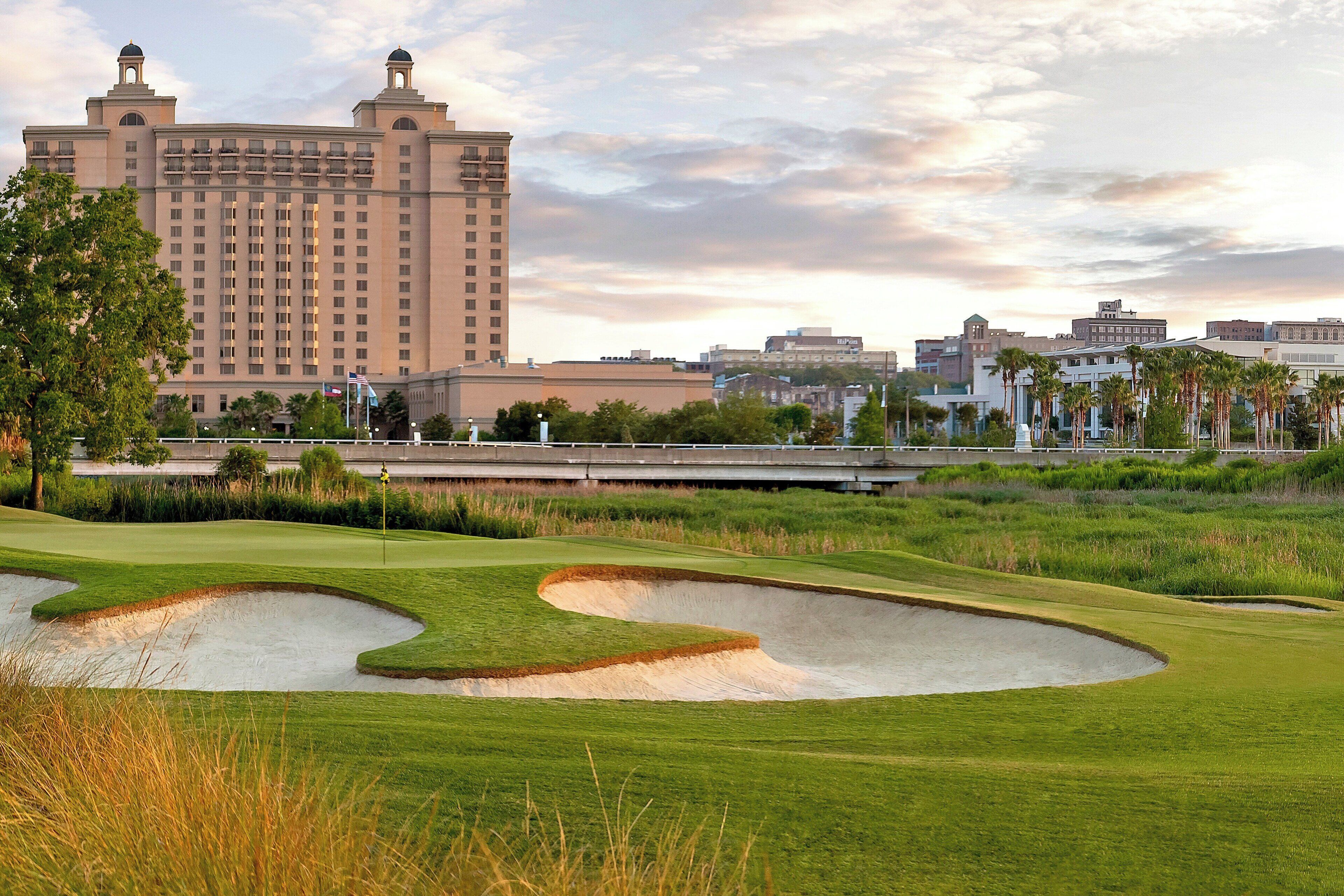 Een golfbaan met bunkers en een groot hotel op de achtergrond.