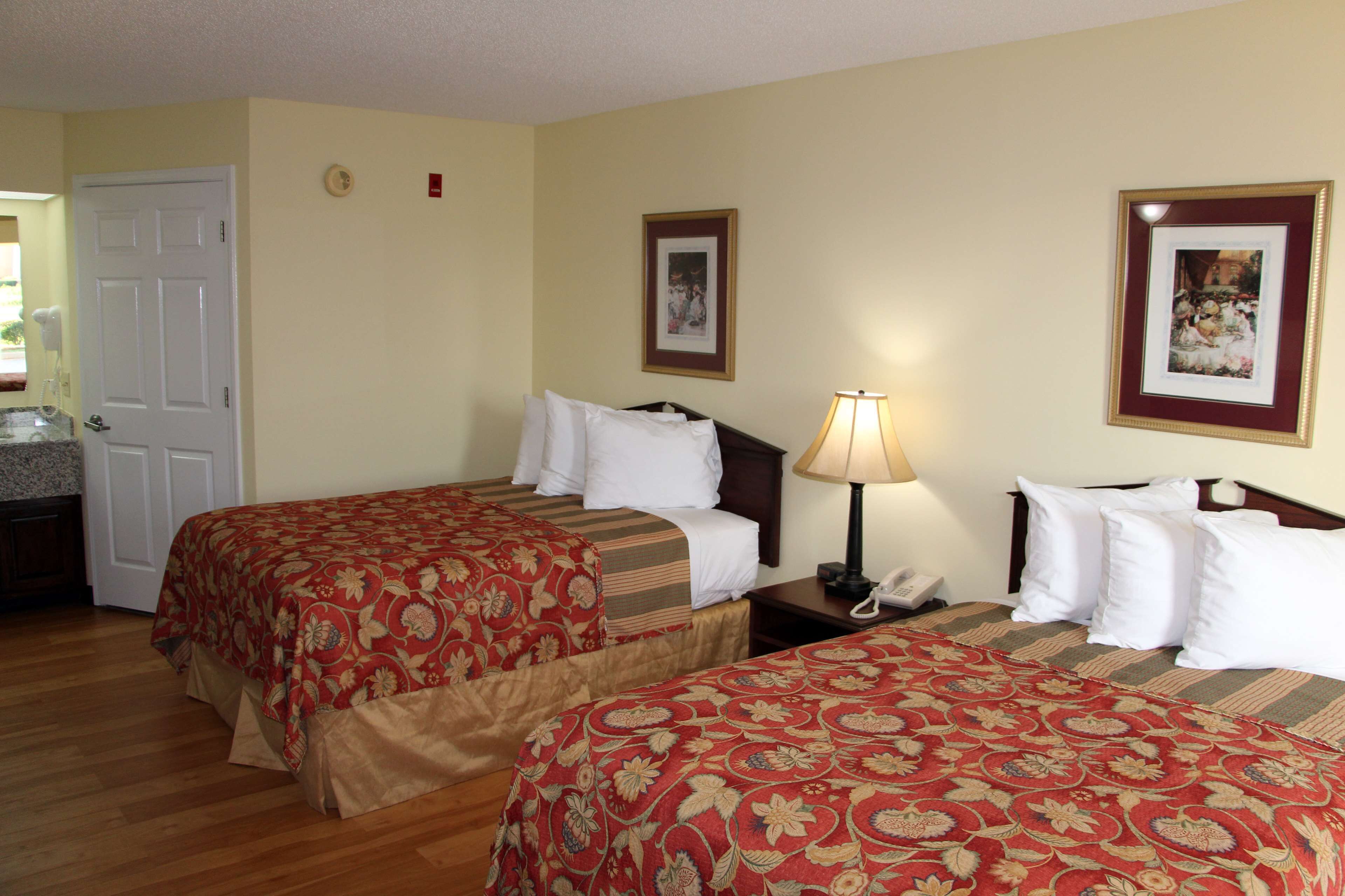A hotel room with two beds, a desk with a lamp, a phone, and framed pictures on the wall.