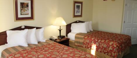 A hotel room with two beds, each with a red floral bedspread, a bedside table with a lamp, and framed pictures on the walls.