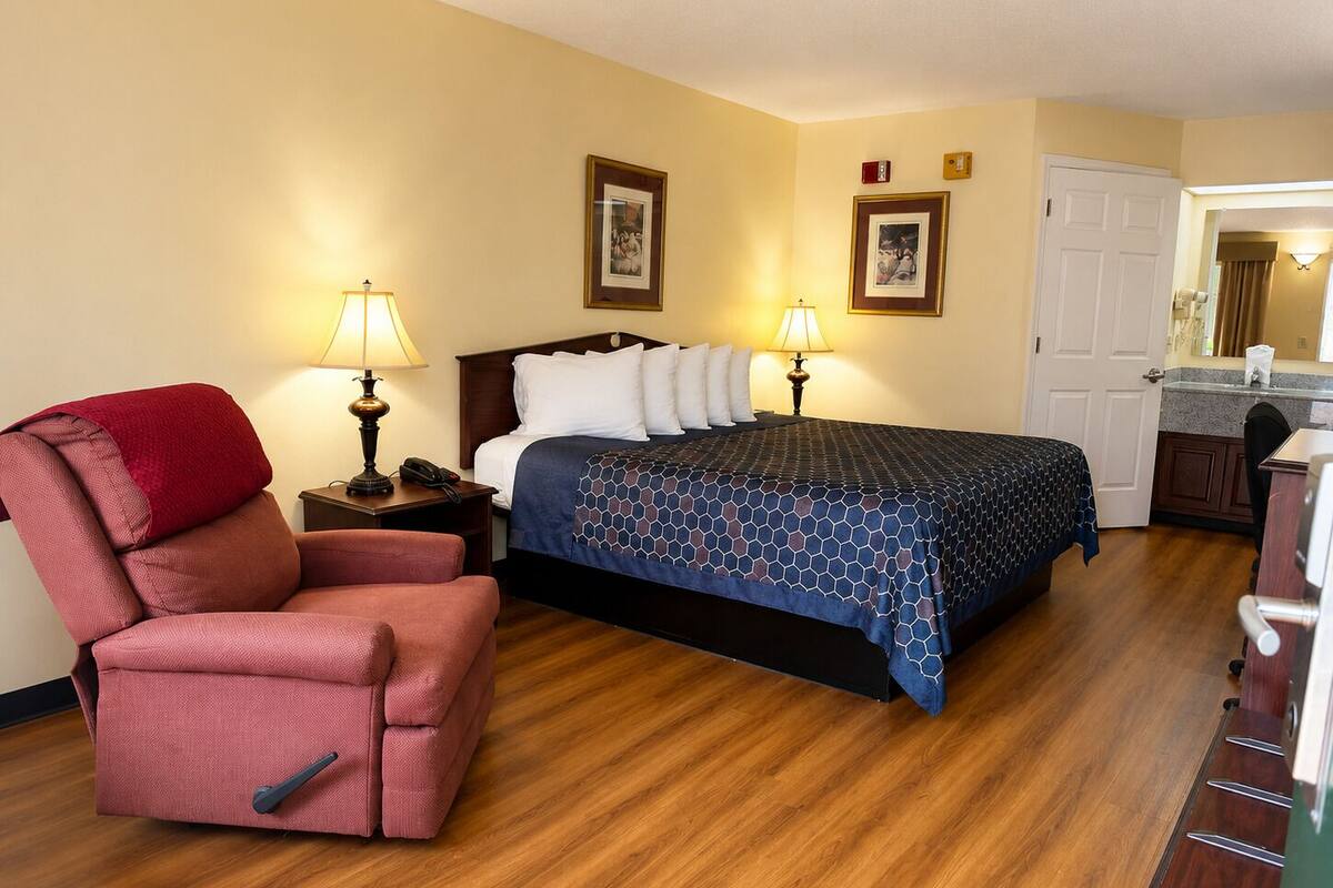 A hotel room with a bed, a chair, two bedside lamps, a wooden floor, and a door.