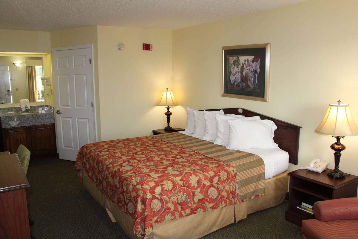 A hotel room with a bed, two bedside tables, a desk, a chair, a mirror, and a painting on the wall.