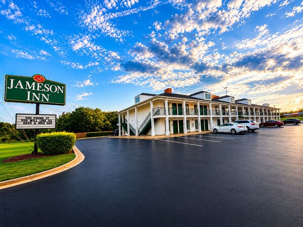A Jameson Inn with a two-story building, a parking lot, and a clear sky with clouds.
