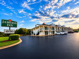 Un Jameson Inn con un edificio de dos pisos, un estacionamiento y cielo despejado con nubes.