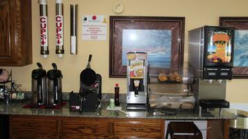 Una cocina de hotel con cafeteras, un dispensador de jugo y un cuadro en la pared.