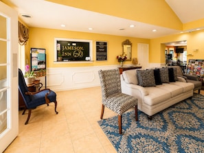 A hotel lobby with a reception desk, a sofa, a patterned armchair, and a coffee table. - Jameson Inn Perry (Perry)