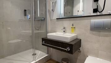 A modern bathroom with a glass-enclosed shower, a vanity with a sink, a mirror, and a toilet.