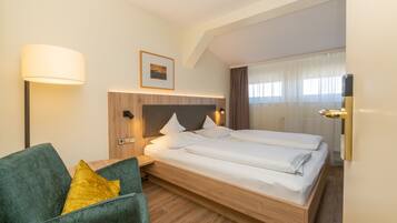Habitació d'hotel amb un llit de fusta, un divanet verd, una taula de nit, una làmpada i una finestra amb cortines.