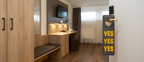 Una habitación de hotel moderna con un armario de madera, un banco, un lavabo pequeño y un espejo.