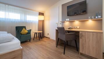 A hotel room with a bed, a desk, a chair, a TV, and a small table.