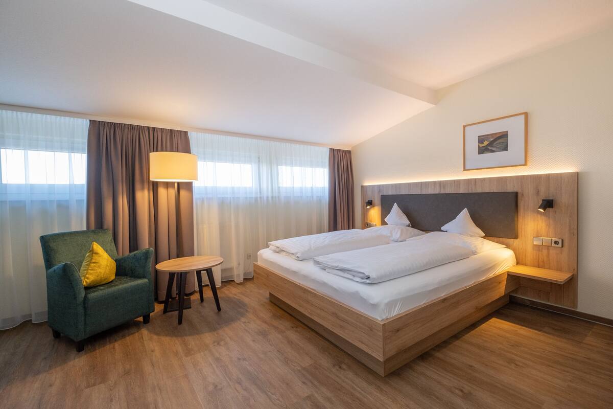 A hotel room with a large bed, a small table, a chair, and a lamp.