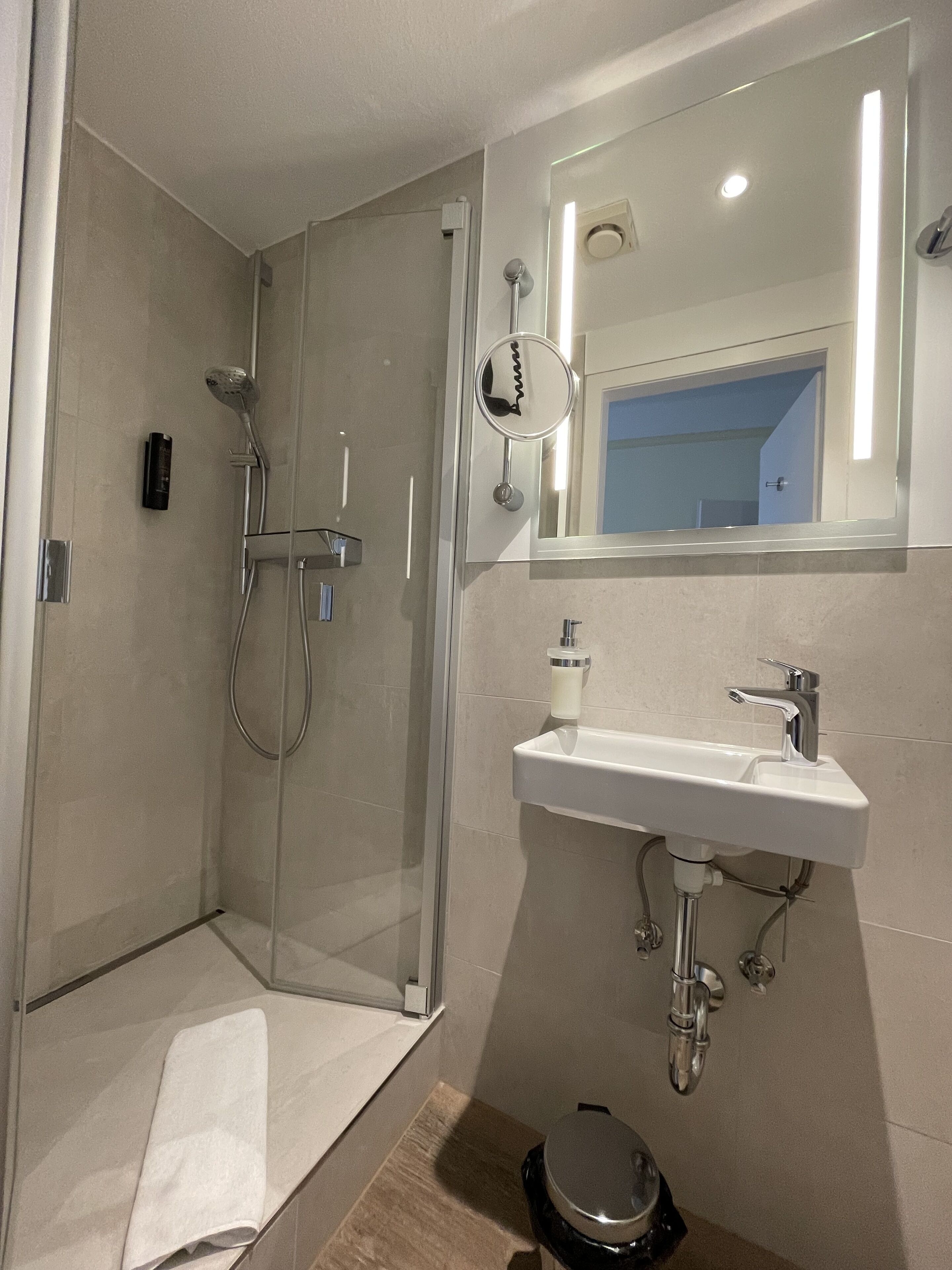 Un baño moderno con ducha de vidrio, lavamanos blanco con espejo y retrete.