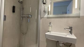 Un baño moderno con ducha de vidrio, lavamanos blanco con espejo y retrete.