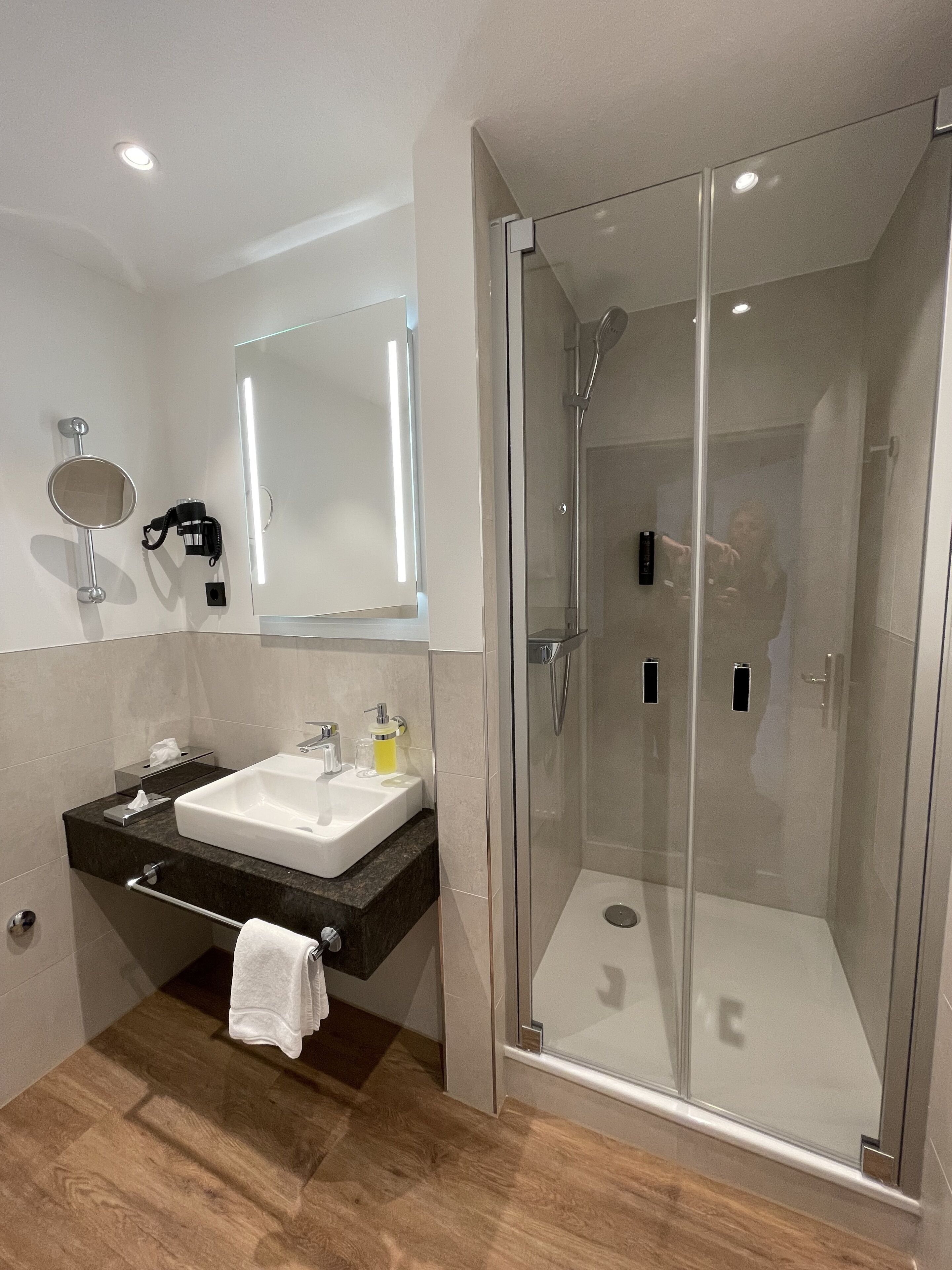 A modern bathroom with a glass-enclosed shower, a vanity with a sink, and a mirror.