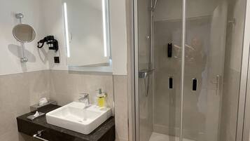 A modern bathroom with a glass-enclosed shower, a vanity with a sink, and a mirror.