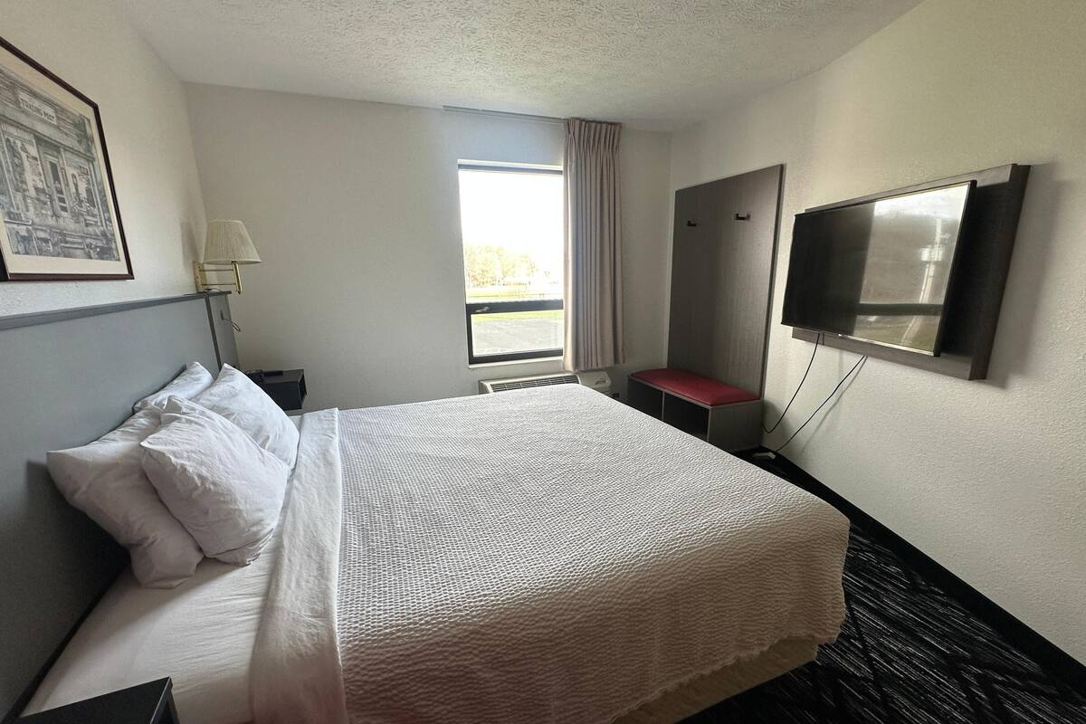 Una habitación de hotel con cama, escritorio, lámpara, televisor y ventana con cortinas.