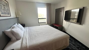 Una habitación de hotel con cama, escritorio, lámpara, televisor y ventana con cortinas.