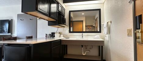 A compact hotel bathroom with a sink, mirror, and a trash bin.