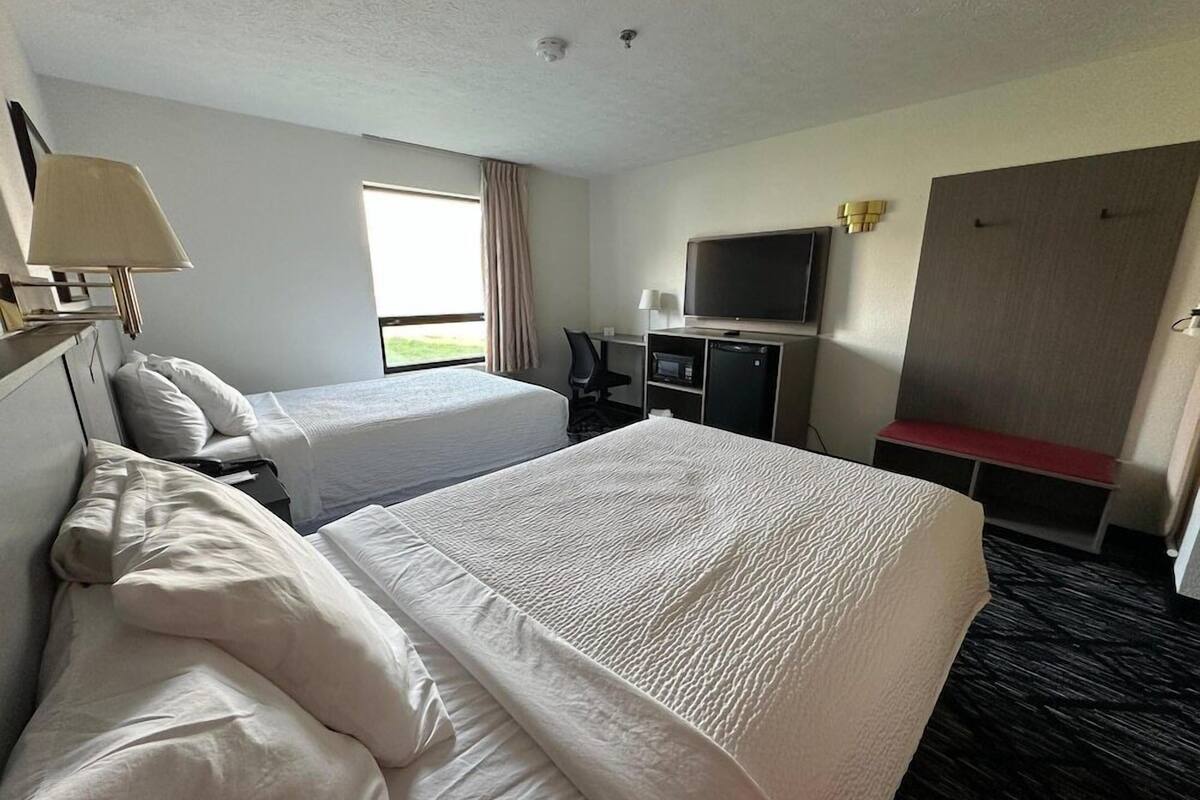Habitación de hotel con dos camas, televisión, escritorio y ventana con cortinas.