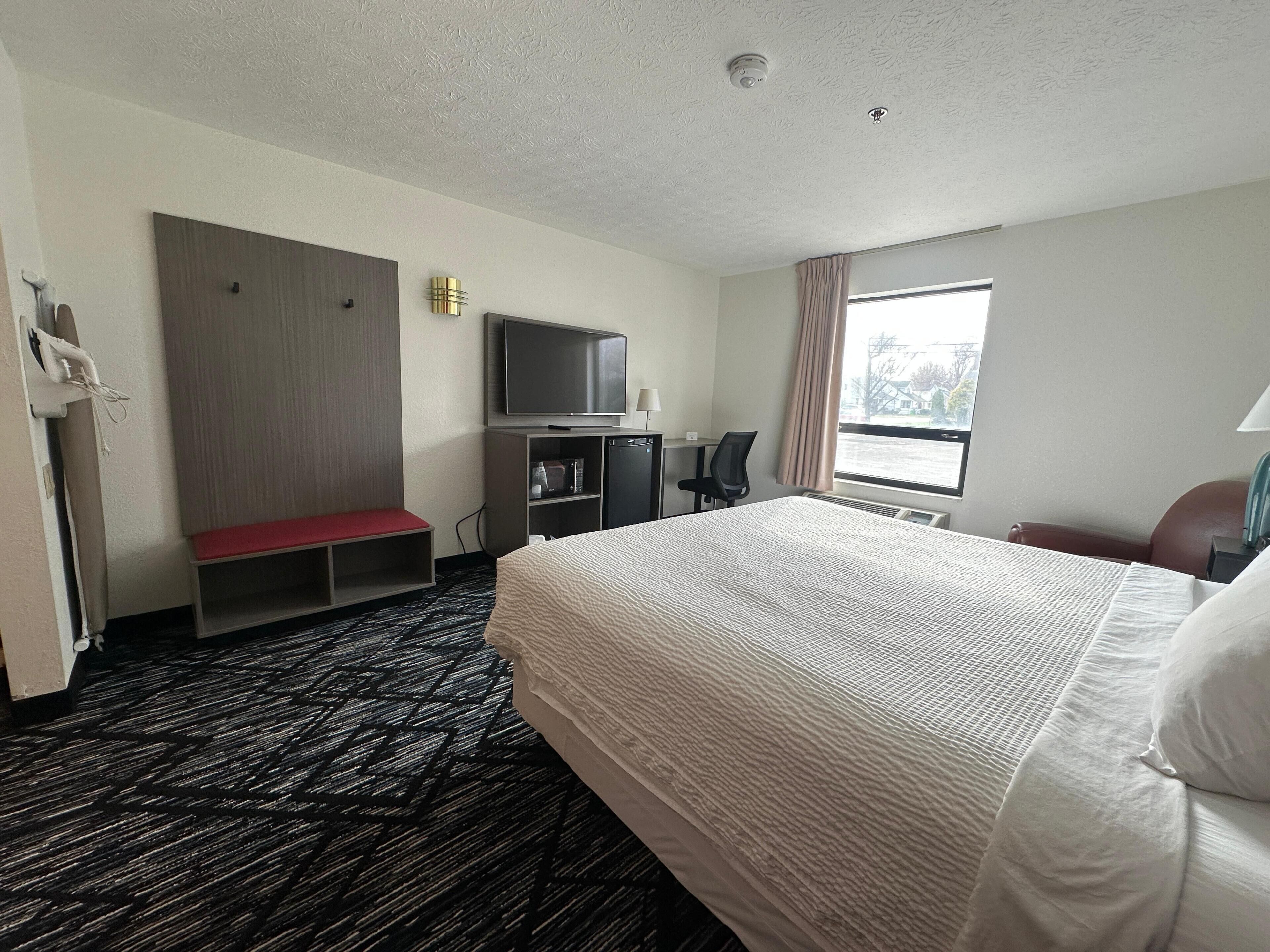 Una habitación de hotel con una cama grande, un escritorio con una silla, un televisor y una ventana con cortinas.