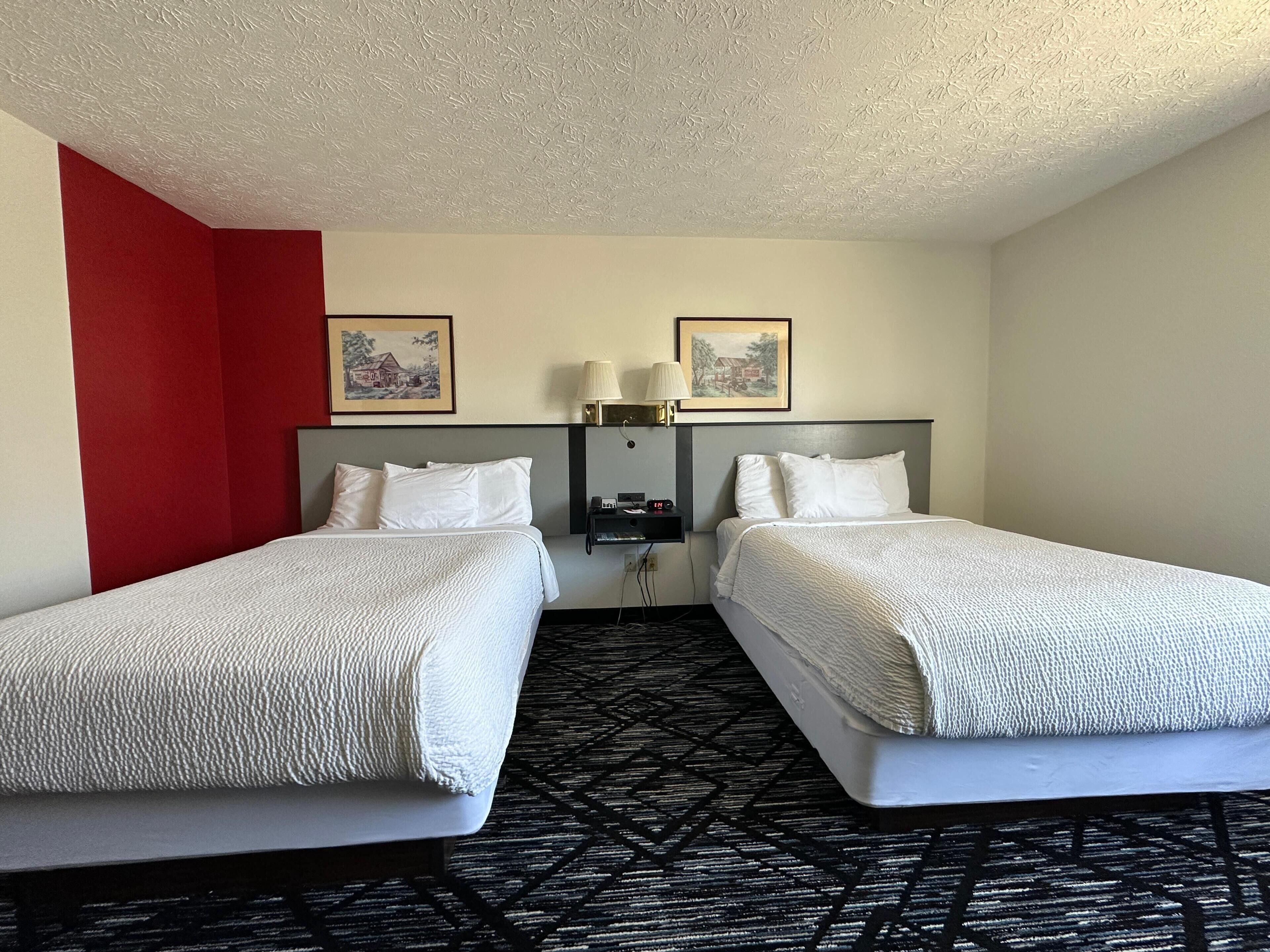 A hotel room with two beds, a red accent wall, and two framed pictures on the wall.