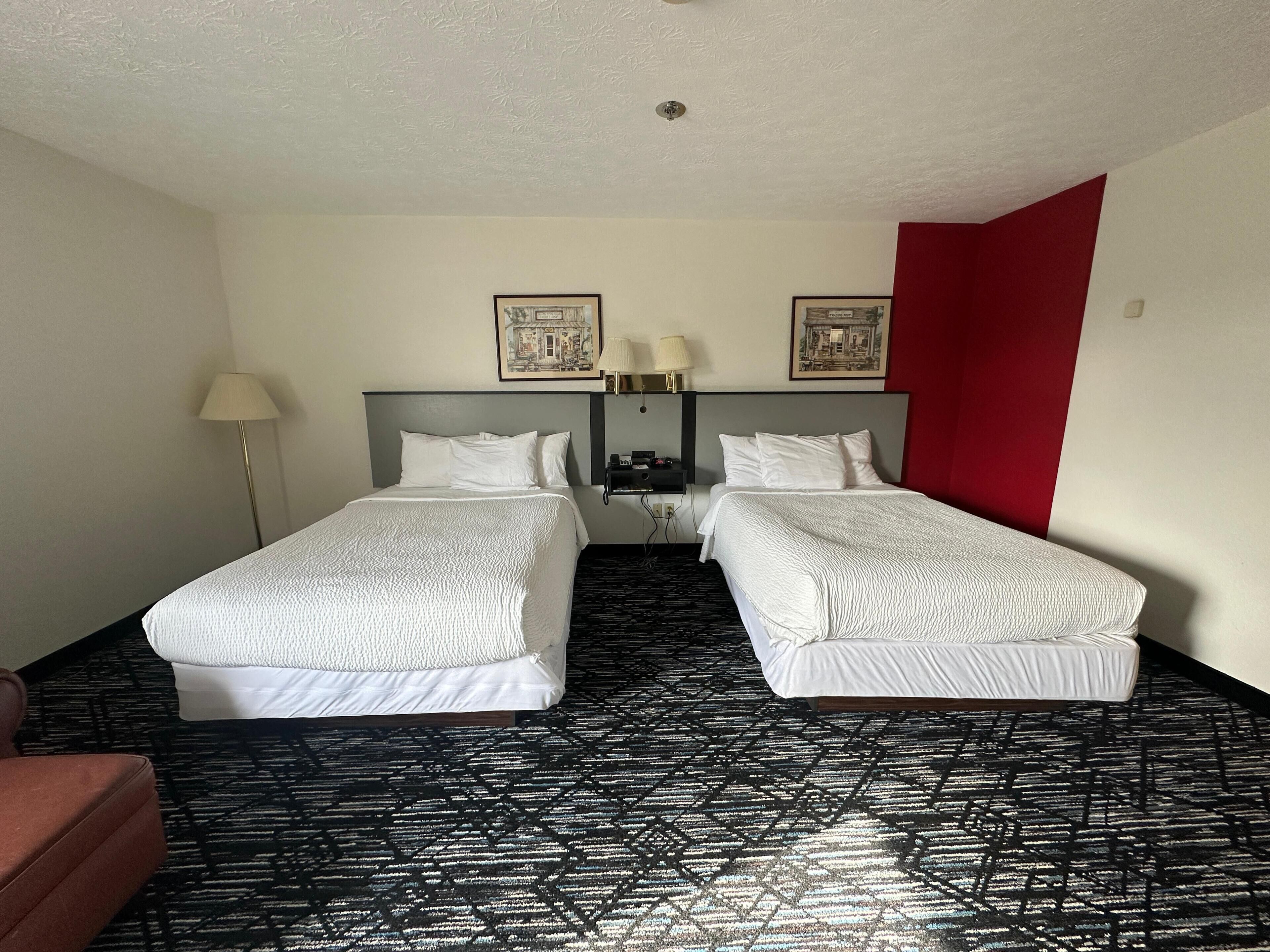 A hotel room with two beds, a red accent wall, a patterned carpet, and a ceiling light.