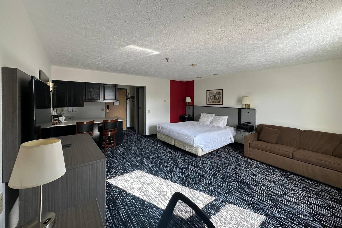 Una habitación de hotel con cama, escritorio, silla, sofá y kitchenette.