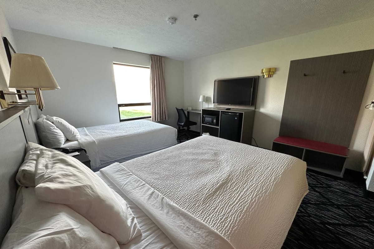 Habitación de hotel con dos camas, televisión, escritorio con computadora y ventana con cortinas.