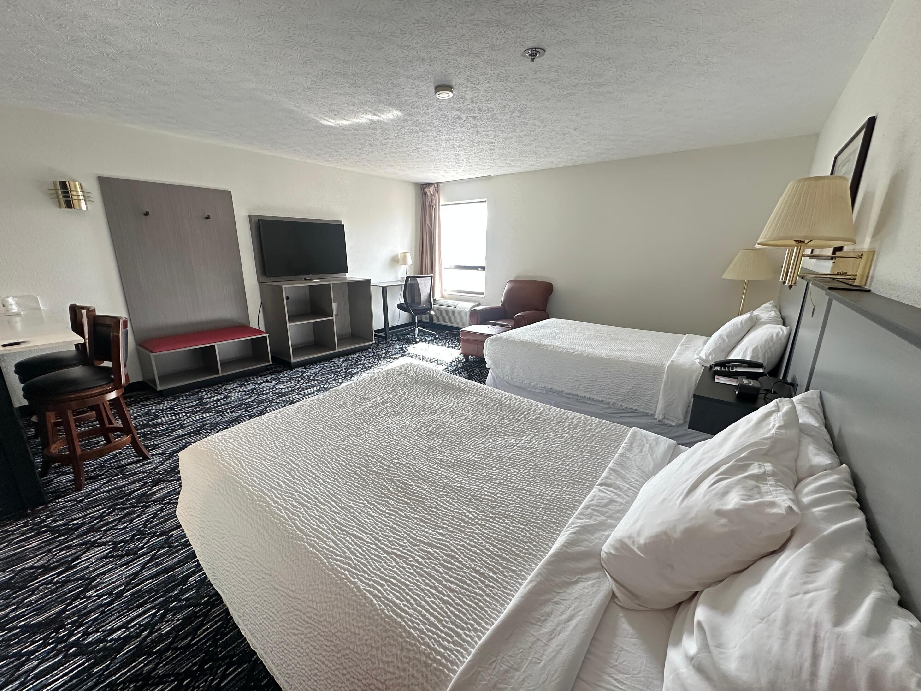 Habitación de hotel con dos camas, un escritorio, un televisor, una silla y una ventana.
