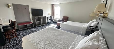 A hotel room with two beds, a desk, a TV, a chair, and a window.