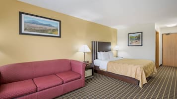 A hotel room with a sofa, a bed, a nightstand, two lamps, and two framed pictures on the walls.