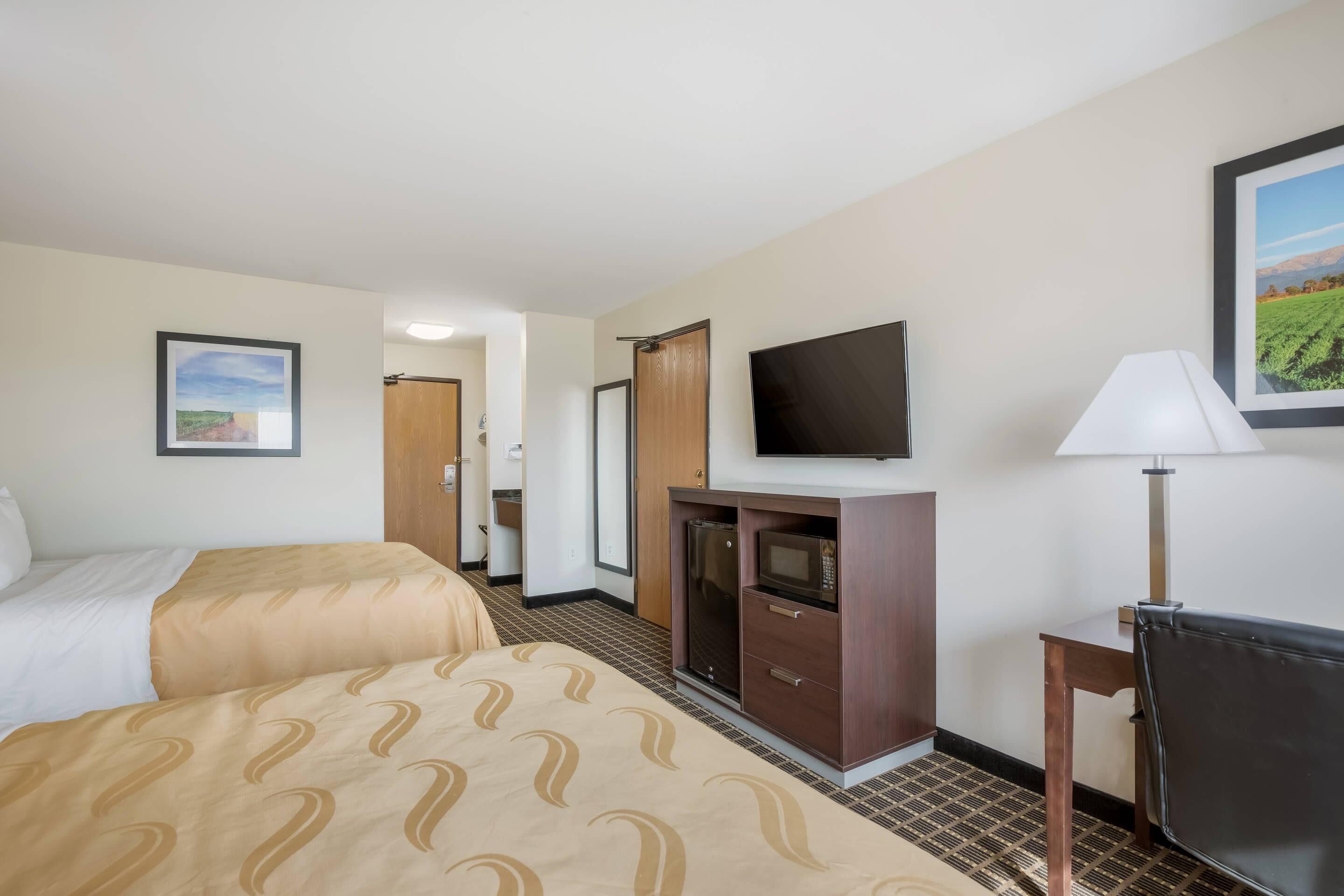 A hotel room with two beds, a TV, a desk with a lamp, and a microwave.