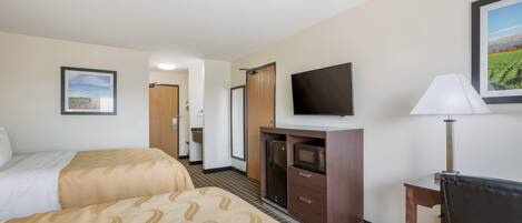 A hotel room with two beds, a TV, a desk with a lamp, and a microwave.