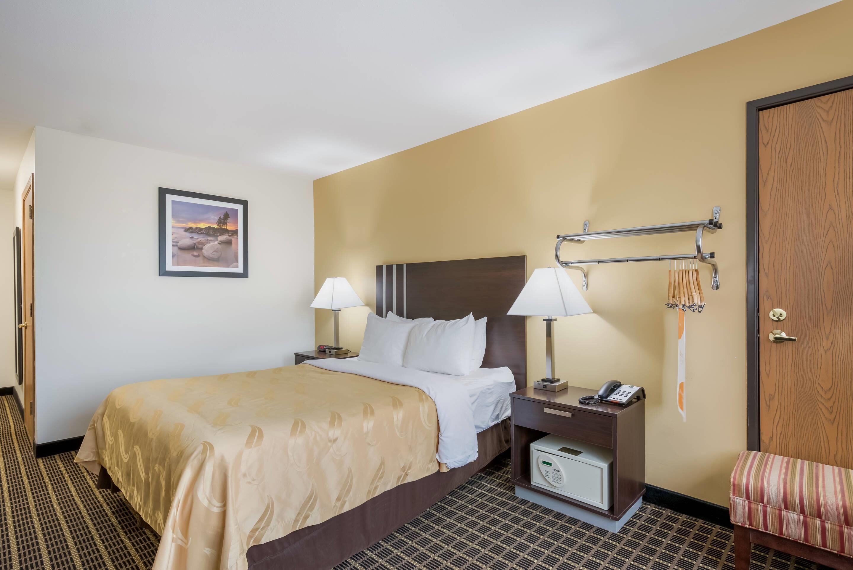 A hotel room with a bed, bedside lamps, a telephone, a small table, a wall-mounted TV, and a door.