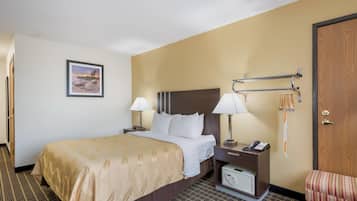 A hotel room with a bed, bedside lamps, a telephone, a small table, a wall-mounted TV, and a door.