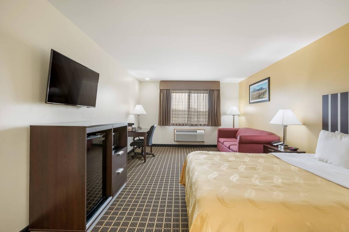 A hotel room with a bed, desk, chair, TV, and a window with curtains.