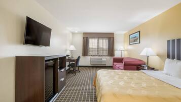Una habitación de hotel con cama, escritorio, silla, televisor y ventana con cortinas.