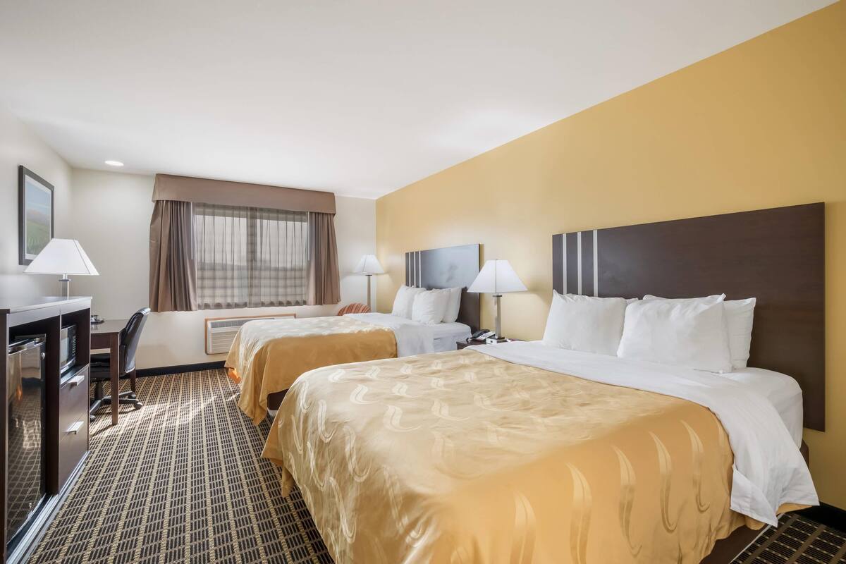 A hotel room with two beds, a desk, a chair, and a window with curtains.