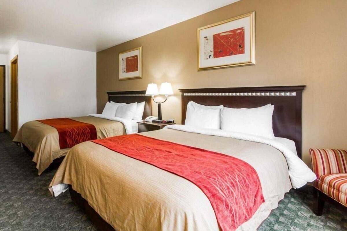 A hotel room with two beds, a nightstand with a lamp, a chair, and artwork on the walls.