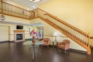 A spacious lobby with a wooden staircase, a fireplace, a round glass table, and striped armchairs.