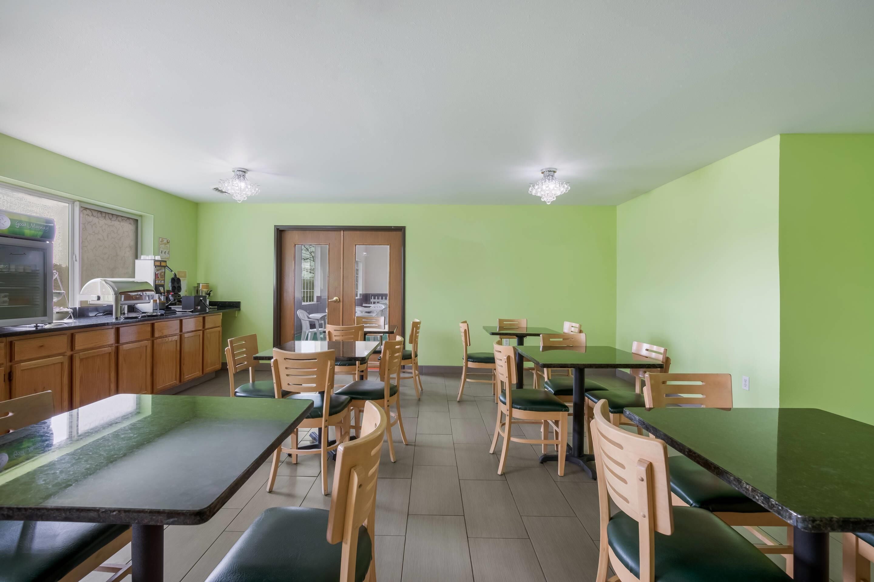 A dining area with wooden tables and chairs, a kitchen area with appliances, and a door leading outside.