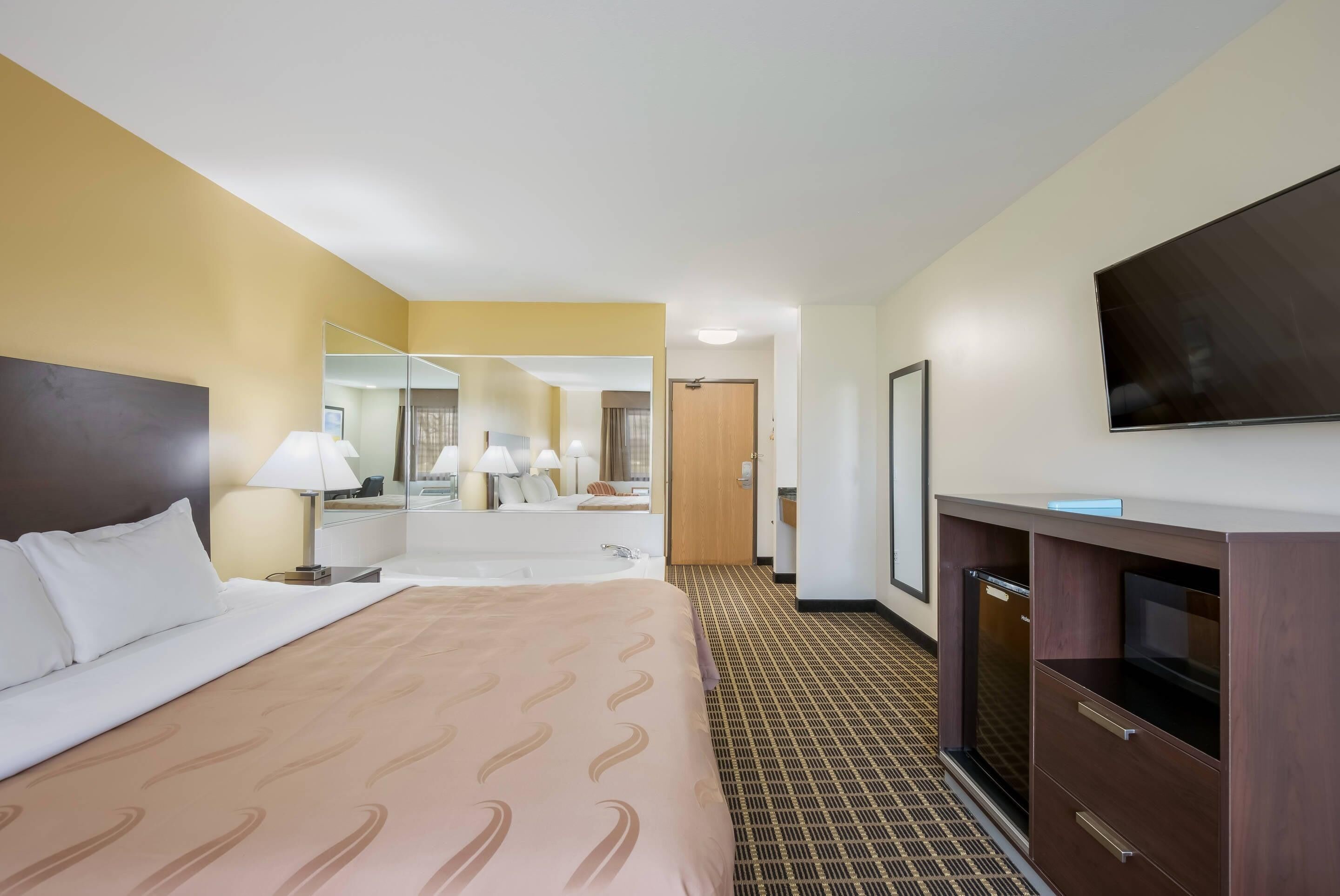 A hotel room with a bed, a TV, a mirror, and a desk.