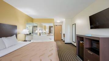 A hotel room with a bed, a TV, a mirror, and a desk.