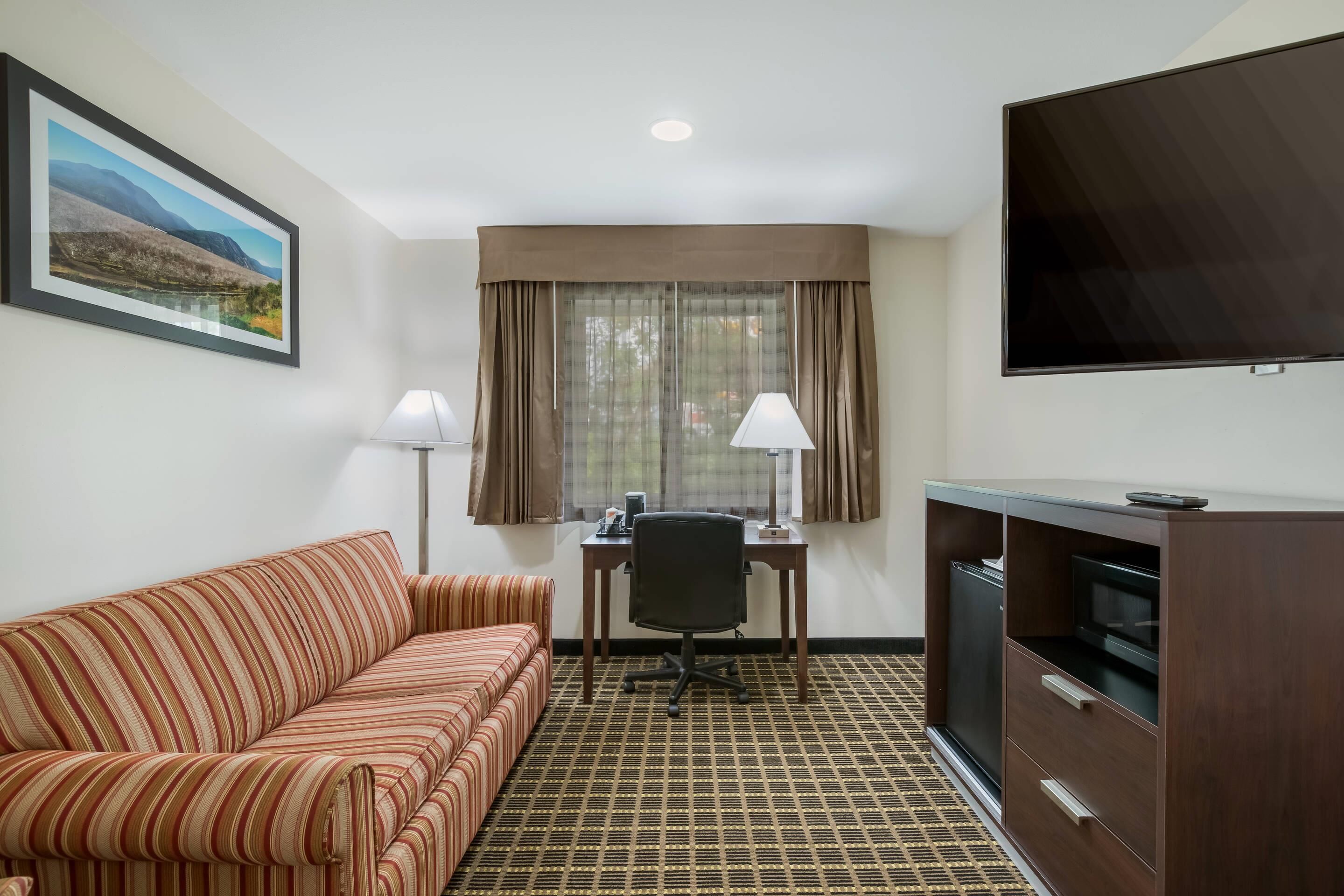 A hotel room with a striped sofa, a desk with a chair, a TV, and a patterned floor.