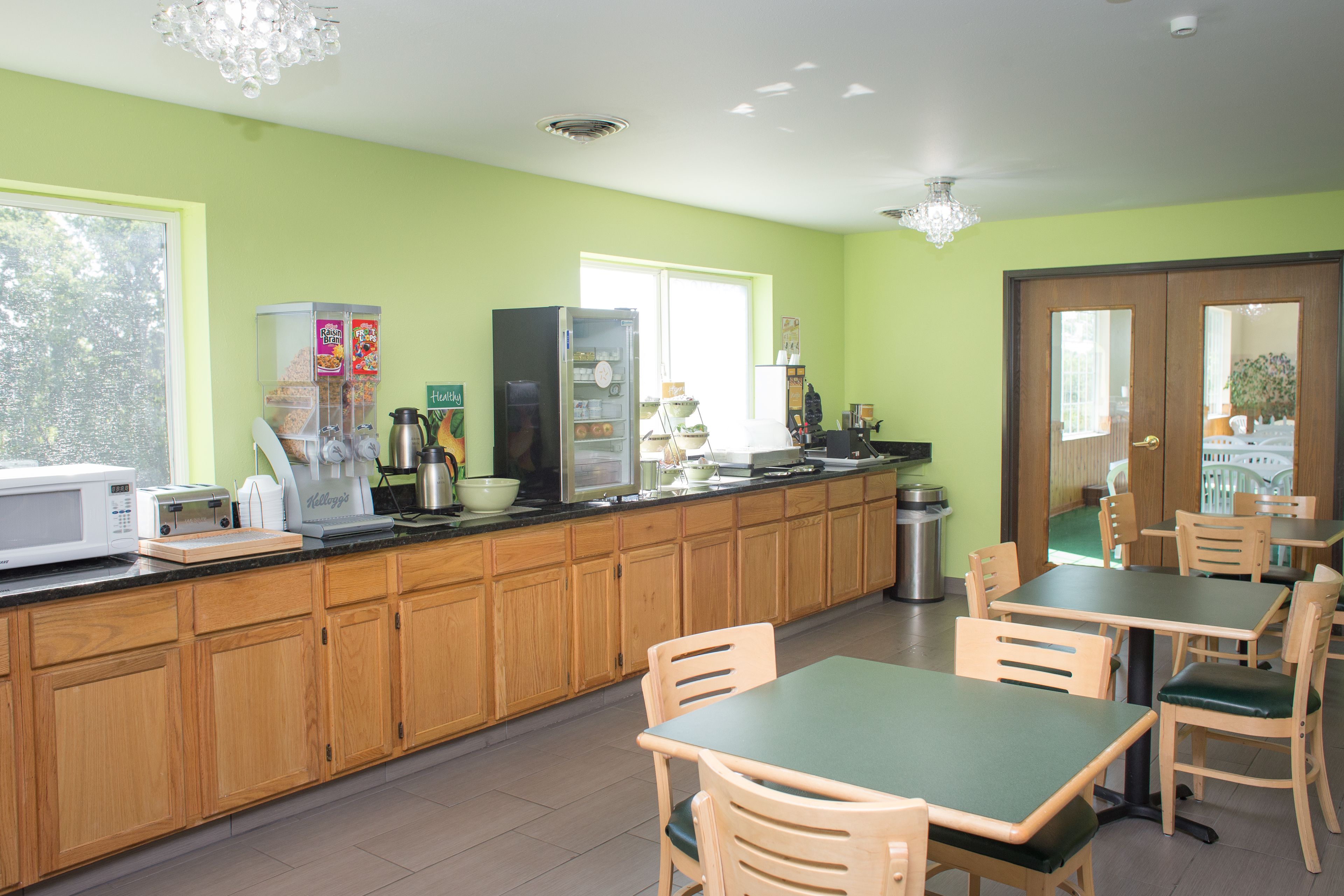 A kitchen with wooden cabinets, a microwave, and a refrigerator. There are wooden chairs and a table with a green tablecloth.
