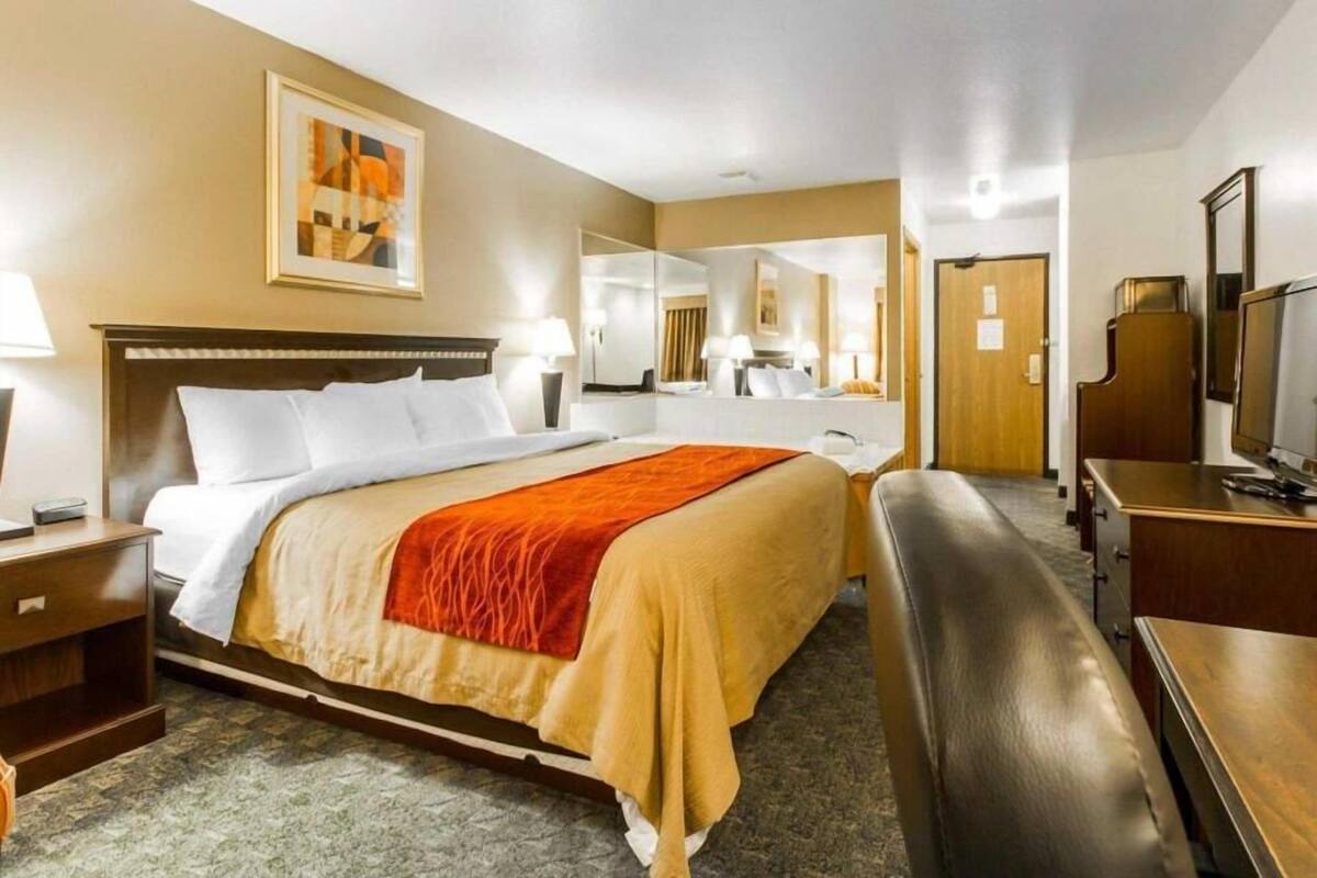 A hotel room with a bed, bedside tables, a desk, a chair, a television, and a mirror.