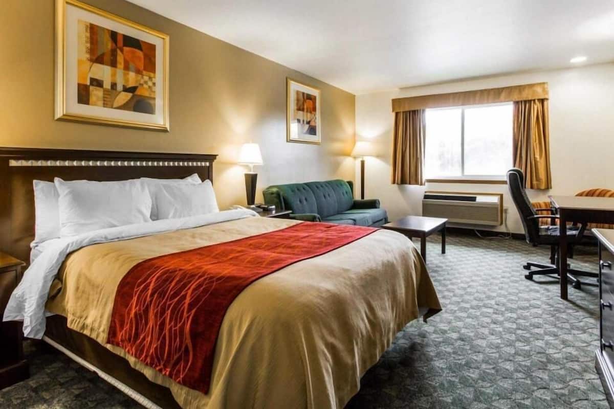 A hotel room with a bed, a desk, a chair, a sofa, a window with curtains, and two wall-mounted lamps.