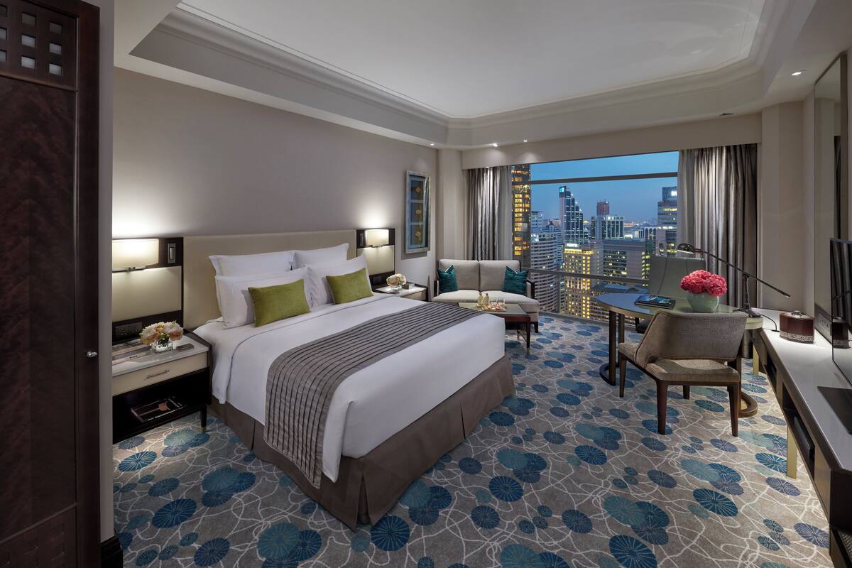 Ein Hotelzimmer mit einem großen Bett, einem Schreibtisch, einem Stuhl und Blick auf die Stadt sowie ein Stadtbild durch das Fenster.